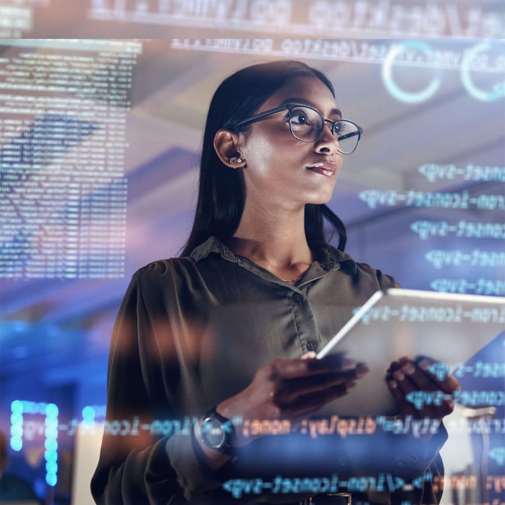 Woman wearing glasses and dark clothing using a tablet, with a wall of programming codes and digital graphics in the background, in a technology or innovation environment