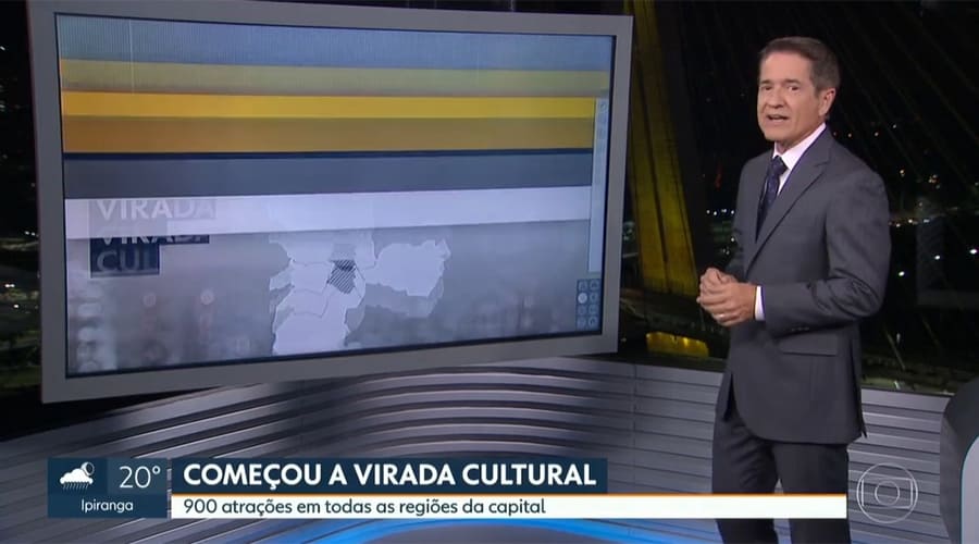 Apresentador de jornal em estúdio mostrando tela com mapa e informações sobre a Virada Cultural em São Paulo.